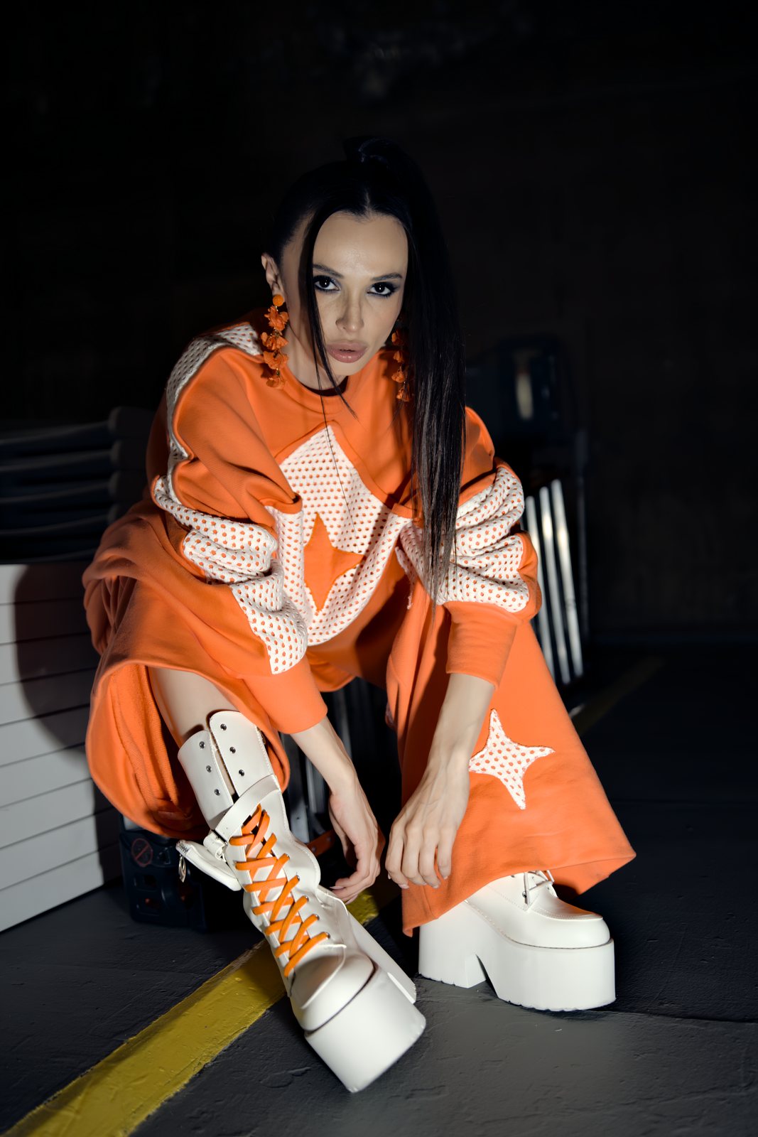 Lala in an orange suit and white platform boots, direct flash