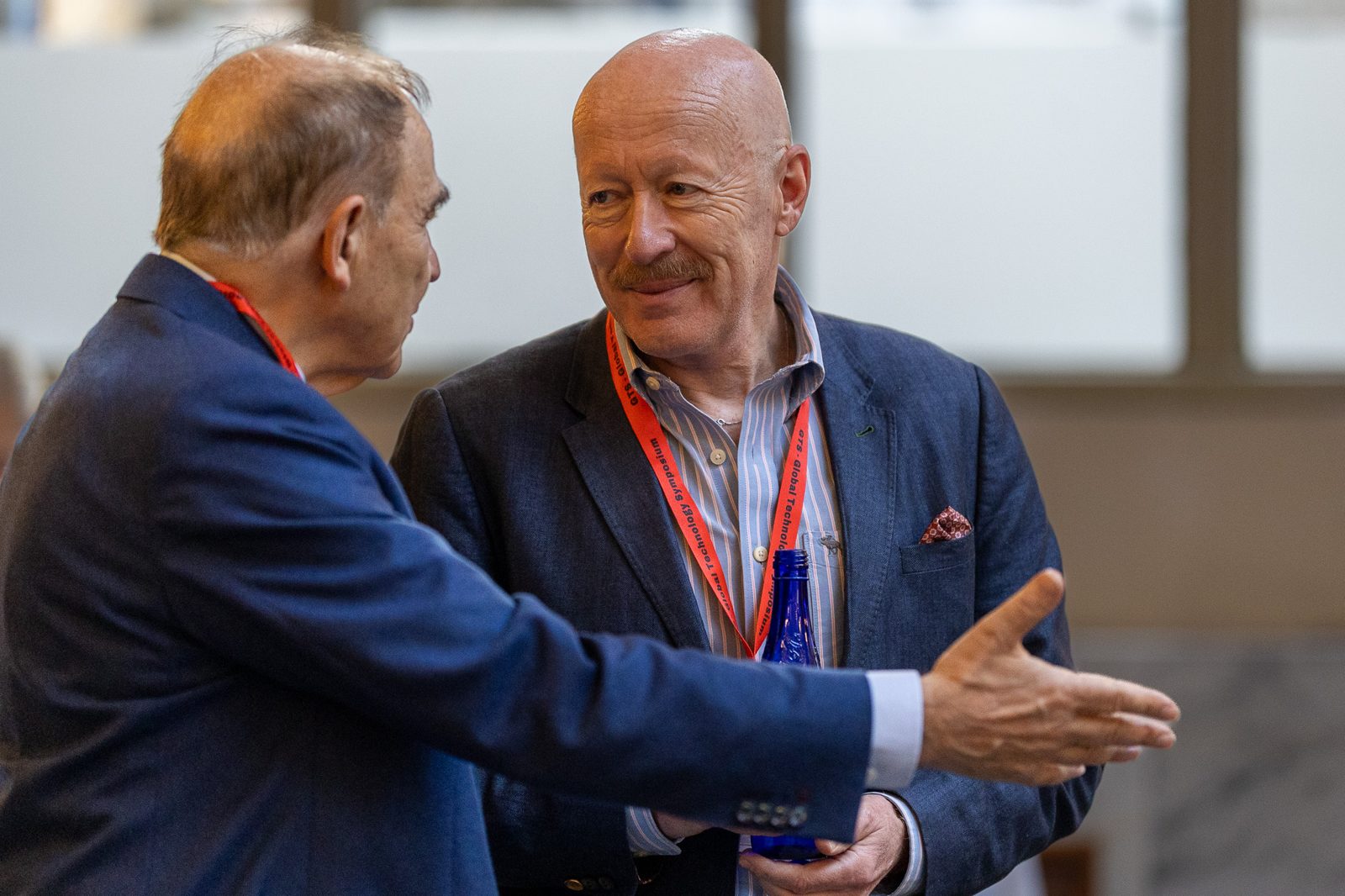 Two men in conversation at a conference, one smiling
