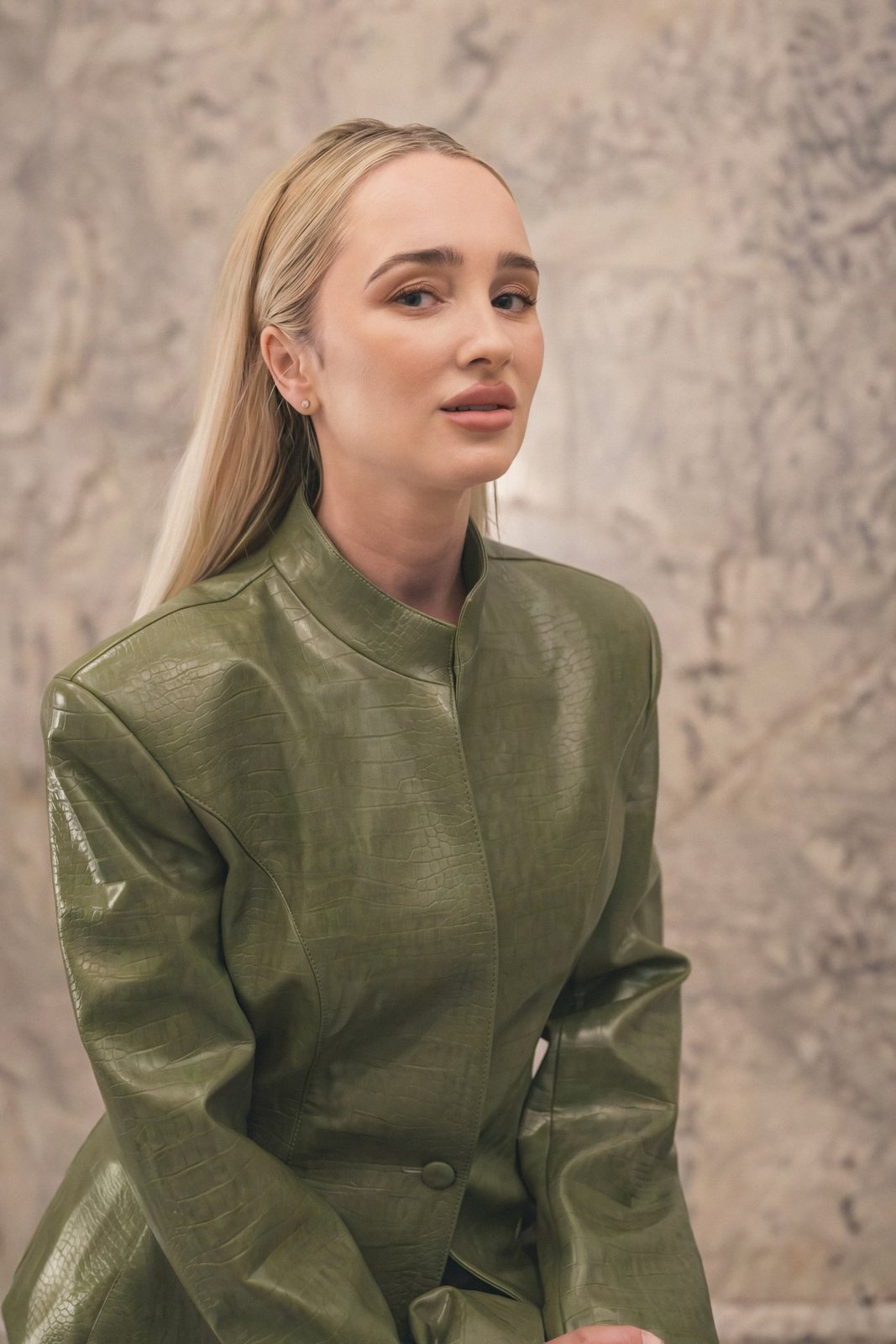 Lera in a green leather jacket against a marble wall, natural light